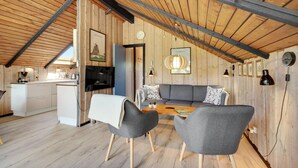 Una acogedora habitación tipo loft con techo de madera, un comedor con mesa y sillas, un sofá con cojines y una kitchenette con estufa y fregadero.