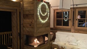 A cozy cabin interior with a wooden fireplace, a sofa, and a small table with a candle.