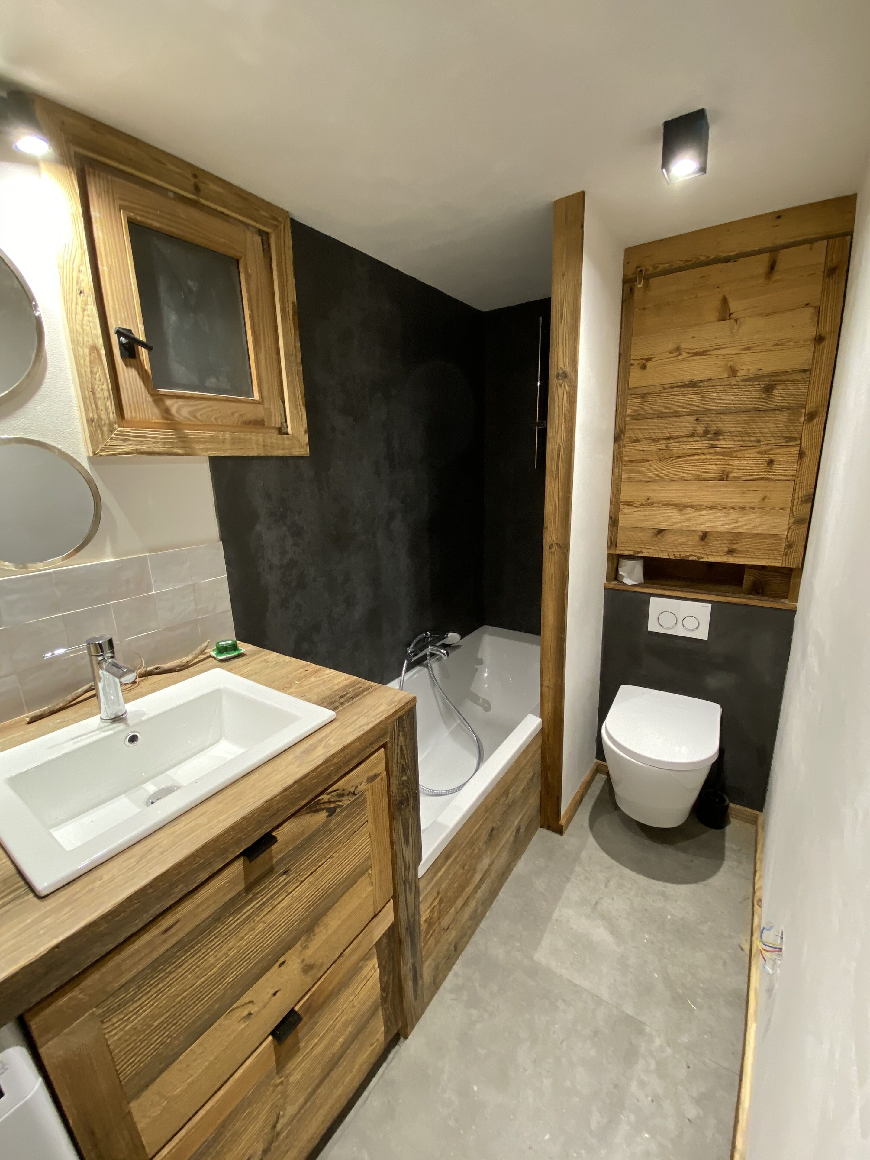 A modern bathroom with a wooden vanity, a bathtub, and a toilet.