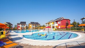 A swimming pool with a fountain, surrounded by colorful buildings and orange umbrellas.