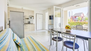 Um apartamento moderno com cozinha compacta, área de refeições com mesa e cadeiras, e varanda com vista para o bairro.