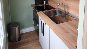 Une cuisine de taille réduite avec des meubles blancs, un plan de travail en bois, un évier en acier inoxydable, un four à micro-ondes et une cuisinière.
