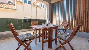 Ein Balkon mit Holztisch und -stühlen, Blick auf ein Gebäude mit Ziegeldächern und einem Holzzaun.