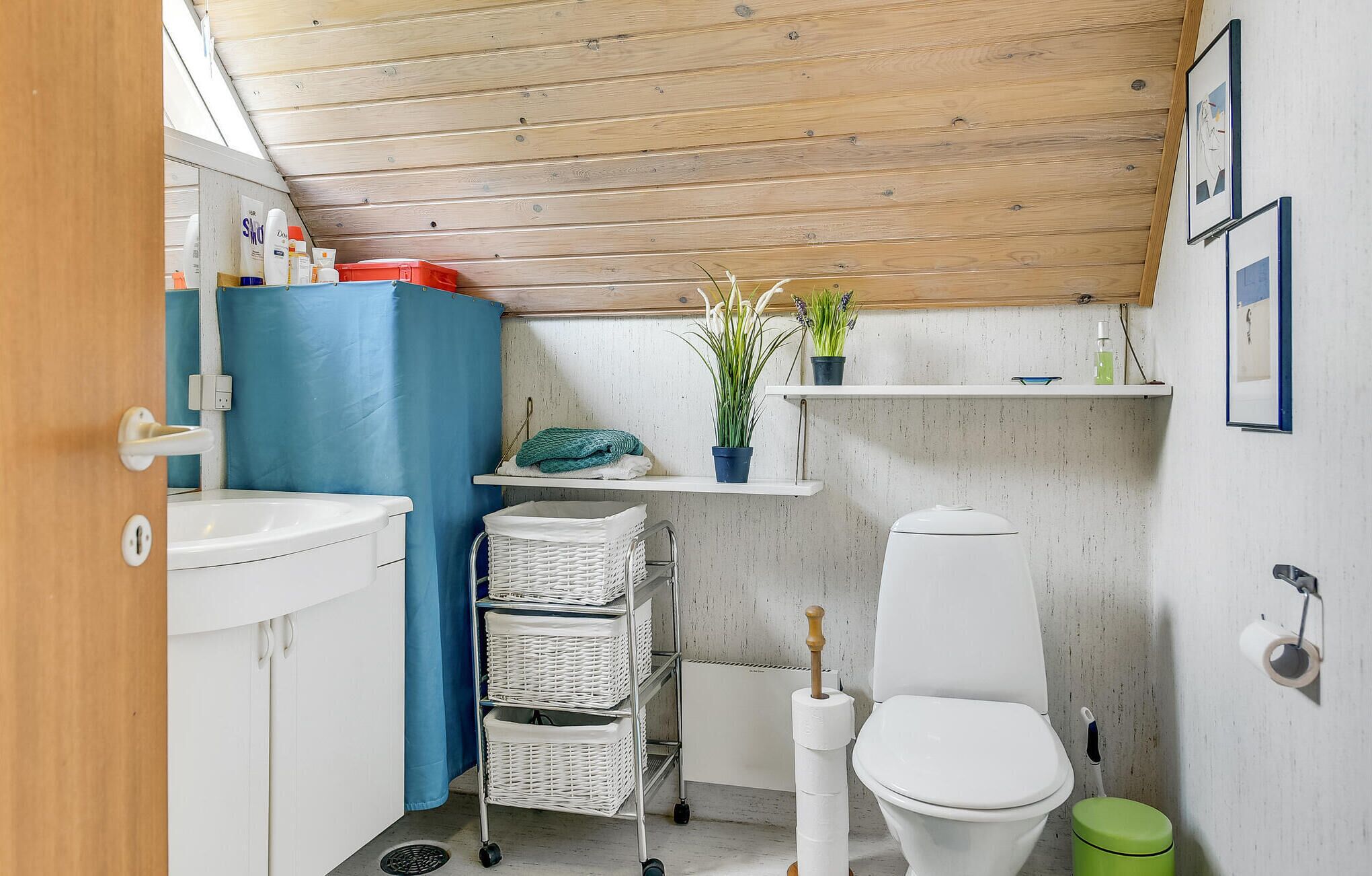 A compact bathroom with a white sink, a toilet, a blue shower curtain, and a small shelf with plants.