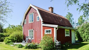 A red wooden house with a sloped roof, a chimney, and a porch with two chairs. - Nice home in Hallstavik with sauna (Hallstavik)
