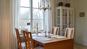 A dining room with a wooden table, chairs, a chandelier, a cabinet with glass doors, and a window with curtains. - Nice home in Hallstavik with sauna (Hallstavik)