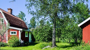 A red wooden house with a sloped roof and a chimney, surrounded by lush green trees and grass. - Nice home in Hallstavik with sauna (Hallstavik)