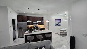 A modern kitchen with a central island, bar stools, and a dining area with a white table and chairs. - Gorgeous build on fresh water canal - very private-heated pool (Cape Coral)
