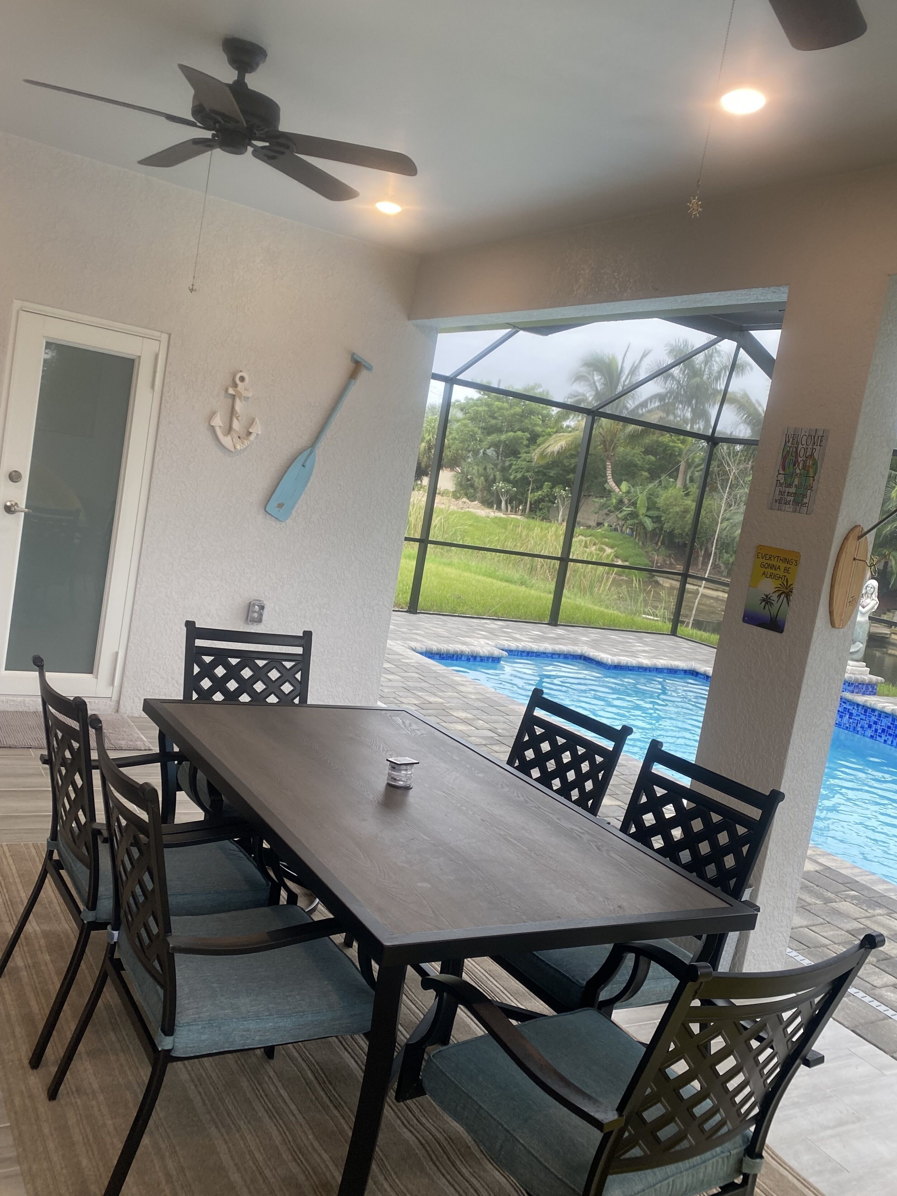 Un coin repas avec une table et des chaises, un ventilateur de plafond et une vue sur une piscine.
