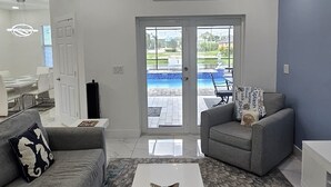 A modern living room with a ceiling fan, a chandelier, a pool view, and a sign reading 'Welcome to Cape Coral.' - Gorgeous build on fresh water canal - very private-heated pool (Cape Coral)