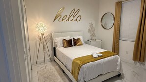 A bedroom with a bed, a bedside table, a lamp, a mirror, and a wall with a 'hello' sign. - Gorgeous build on fresh water canal - very private-heated pool (Cape Coral)