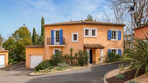 A two-story building with a tiled roof, a balcony with black railings, and a small garden area with various plants. - Lovely home in Fayence (Fayence)