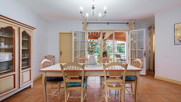 A dining area with a wooden table and chairs, a chandelier, and a view of the outdoors. - Lovely home in Fayence (Fayence)