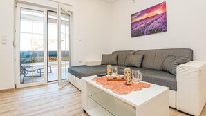 Ett modernt vardagsrum med en grå soffa, ett vitt soffbord med en underlägg och en tavla som föreställer ett lila fält på väggen.