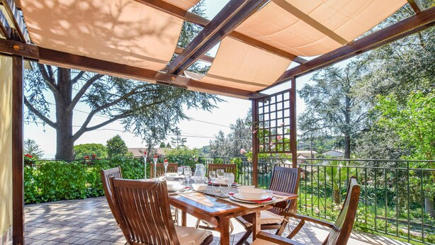 An outdoor patio with a wooden table and chairs, a pergola providing shade, and a view of greenery and trees. - Amazing apartment in Trecastagni with WiFi (Trecastagni)