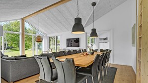 Et moderne spiseområde med et stort træbord, sorte stole og hængende lys.