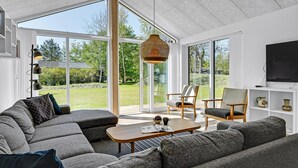 En moderne stue med en stor krogsofa, et træsofabord og et fjernsyn på væggen.