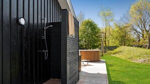 Et moderne udendørs bruseområde med træterrasse, jacuzzi og græslignende landskab.