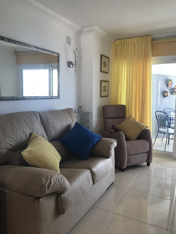 A living room with a beige sofa, a brown armchair, and a yellow curtain.
