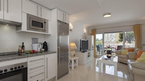 Una cucina moderna con elettrodomestici in acciaio inox, una zona pranzo con tavolo e sedie, e un soggiorno con divano e televisore.