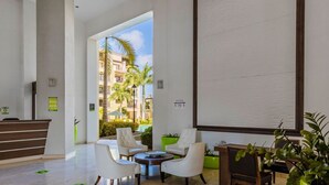 A spacious lobby with a reception desk, seating area, and a large window offering a view of palm trees and buildings.