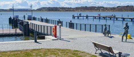 Paseo marítimo frente al agua con un banco de madera, una estatua y un cartel que dice "HAFEN SELLIN".