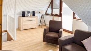 A cozy loft bedroom with a wooden floor, a brown armchair, a small sofa, and a wooden dresser with speakers. - Beach front home in Mariendorf with WiFi (Mariendorf)