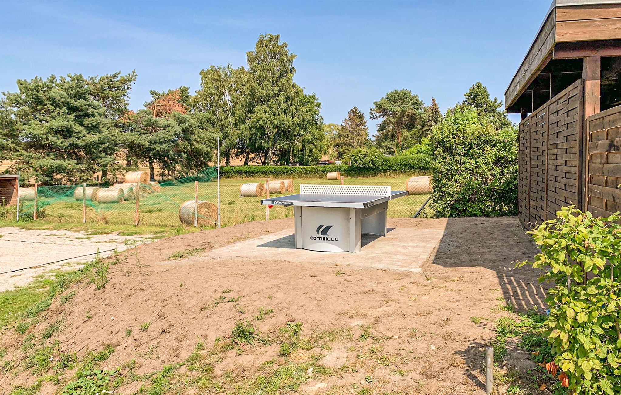 A ping pong table in an outdoor area with hay bales and trees in the background.
