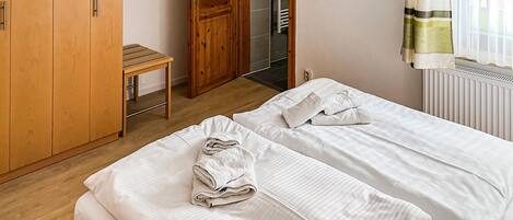 A bedroom with two single beds, a wooden wardrobe, a small table, and a mirror.