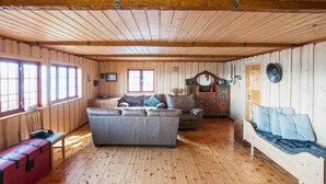 Interior acogedor de una cabaña con paredes y suelos de madera, un sofá, un banco y un aparador.