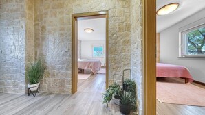 A room with stone walls, a wooden floor, a bed with a pink bedspread, and a window with a view of trees. - Beach front home in Pridraga (Pridraga)