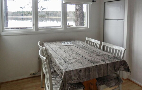 Un coin repas avec une table en bois rustique, des chaises blanches et une vue sur un lac, visible à travers de grandes fenêtres.