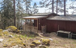 A rustic cabin with a wooden deck and a metal roof, surrounded by trees and rocks. - Nice home in Herräng with sauna (Herräng)
