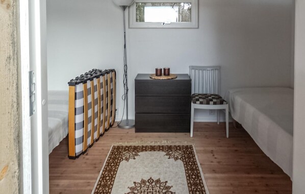 Une petite pièce bien éclairée, avec un lit, une chaise, une commode et un radiateur.