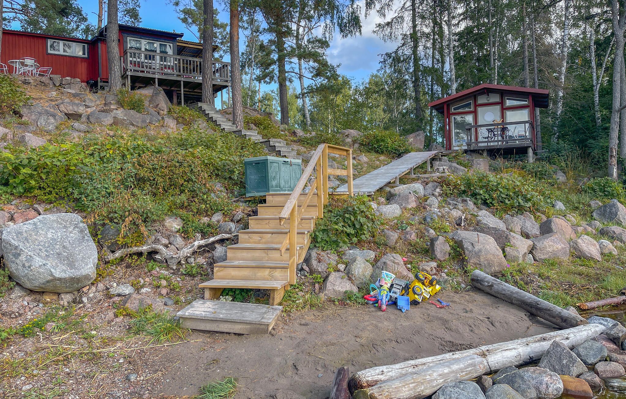 Un escalier en bois mène à un chalet doté d’une terrasse, qui est entouré d’arbres et de rochers.