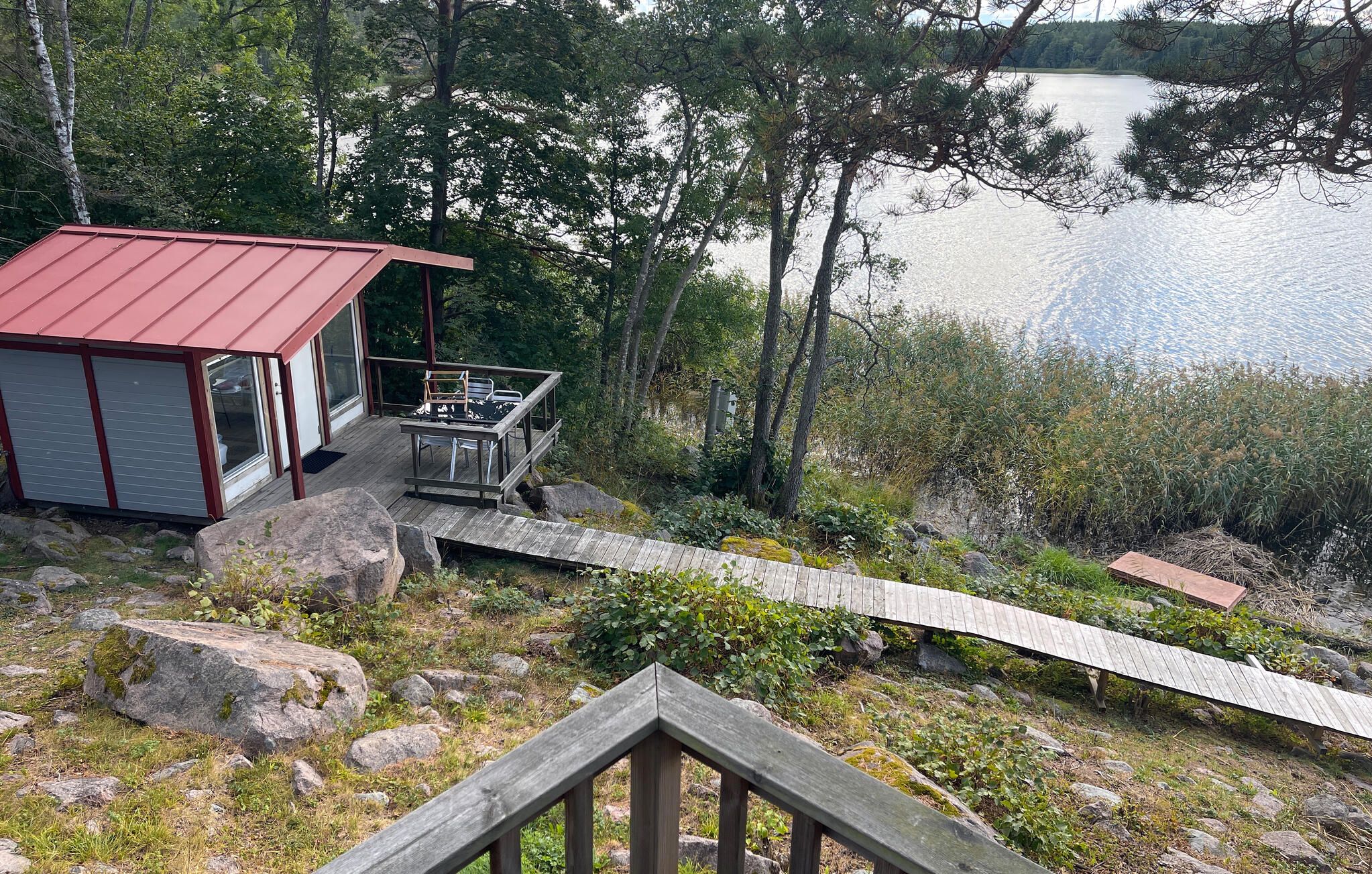 Une cabane dotée d’une terrasse donnant sur un lac, entourée d’arbres et de rochers.
