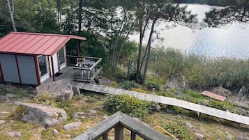 Eine Holzhütte mit einer Terrasse mit Blick auf einen See, umgeben von Bäumen und Felsen.