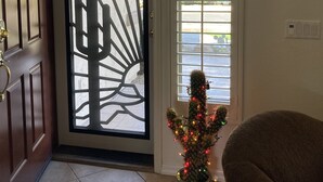 Una puerta con una verja metálica decorativa, una planta en maceta con luces y una ventana con persianas.