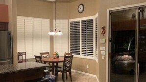 Una cocina con comedor, un reloj y un ventanal corredero que da a un patio.