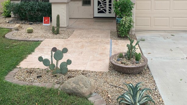 Una casa de color beige, con garaje y un jardín delantero con cactus y plantas.