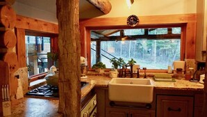 Eine rustikale Küche mit Holzbalken, einem großen Fenster und Blick auf den Wald.