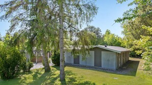 A single-story building with a sloped roof, surrounded by a well-maintained lawn and trees. - Pet friendly home in Væggerløse (Væggerløse)