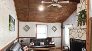 A living room with a stone fireplace, a ceiling fan, and a large window. - Hummingbird Cabin, located down Riverroad close to local shops and restaurants! (Concan)
