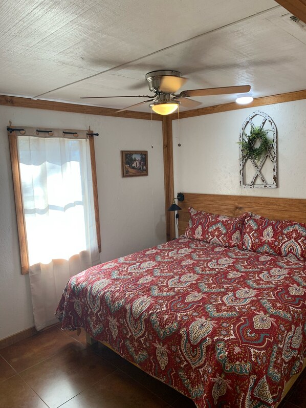 A bedroom with a bed, a ceiling fan, a window with curtains, a wall-mounted plant, and a framed picture. - Hummingbird Cabin, located down Riverroad close to local shops and restaurants! (Concan)