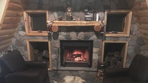 A cozy living room with a stone fireplace, two leather armchairs, and a fur rug. - Honey dome Hideout Unique cabin sitting on 5 acres in northern Michigan (Lewiston)