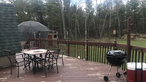 A wooden deck with a table and chairs, a barbecue grill, and a cooler. - Honey dome Hideout Unique cabin sitting on 5 acres in northern Michigan (Lewiston)
