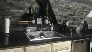 A kitchen with a black countertop, a stainless steel sink, and a dishwasher. There are potted plants on the counter and a sign that reads "Our Adventure Fund". - Honey dome Hideout Unique cabin sitting on 5 acres in northern Michigan (Lewiston)