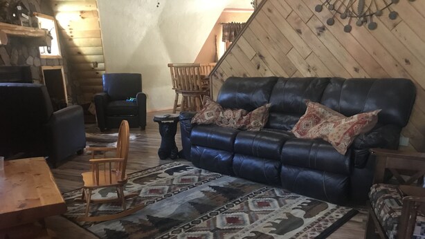 A cozy log cabin interior with a leather sofa, wooden chairs, a patterned rug, and a stone fireplace. - Honey dome Hideout Unique cabin sitting on 5 acres in northern Michigan (Lewiston)
