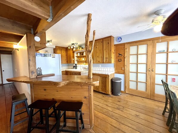 Una cocina rústica con armarios de madera, una barra con taburetes y un ventanal amplio.