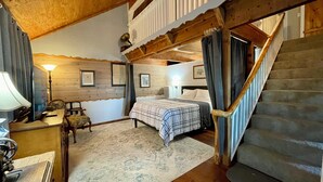 Ein gemütliches Schlafzimmer mit einem Bett, einem Schreibtisch mit Lampe, einem Sessel und einer Treppe.